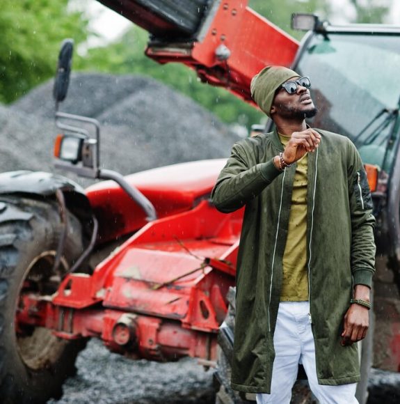 stylish-african-american-man-hat-sunglasses-posed-outdoor-rain-against-tractor-with-bucket_627829-442
